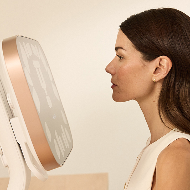 Woman in profile gazing at a rose-gold medical/beauty device with a large circular screen on a stand
