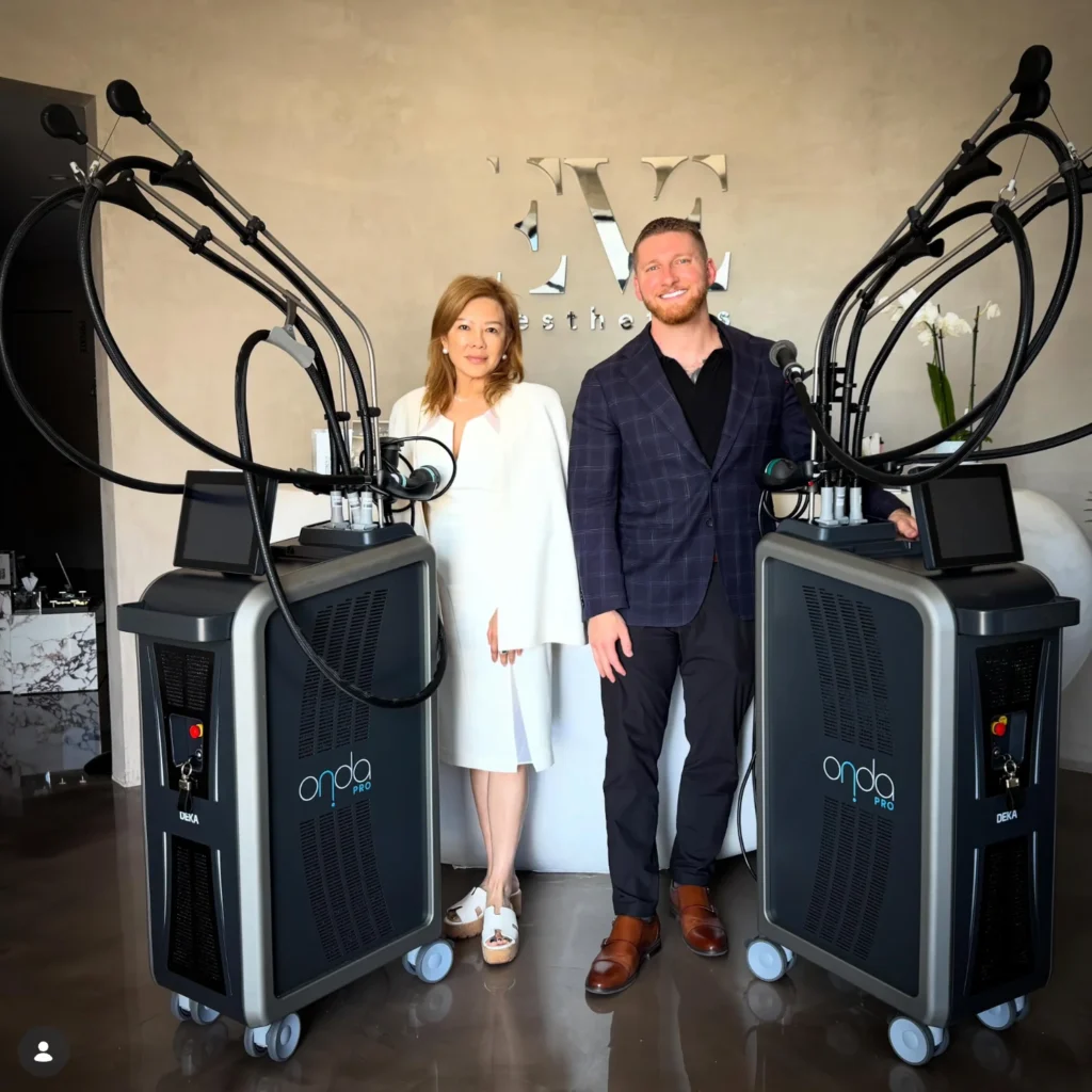 Two professionals stand beside large medical devices labeled 'ondo pro' in a modern clinic studio setting, smiling at the camera.