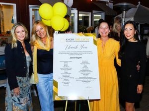 Four women smile and pose with a large 'Thank You' board at a Know The Glow charity event, yellow balloons in the background.